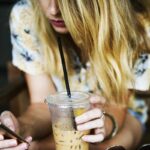 ragazza con il cellulare in mano e un frullato nell'altra mano