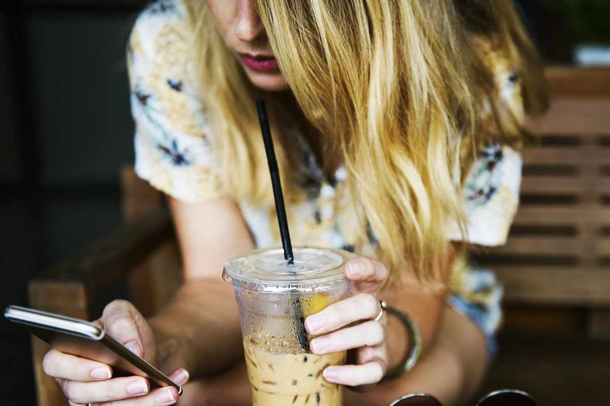 ragazza con il cellulare in mano e un frullato nell'altra mano